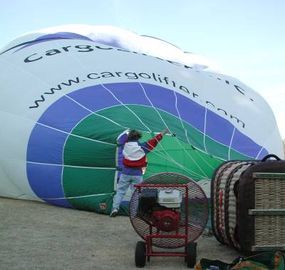 A man holds the balloon steady as it’s inflated with a large red metal fan.