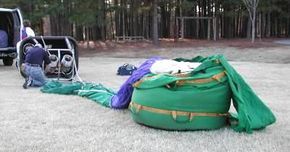 A man starts preparing a green and purple hot air balloon for launch.