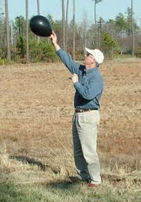 A man holds a small black balloon above his head to gauge the wind direction.