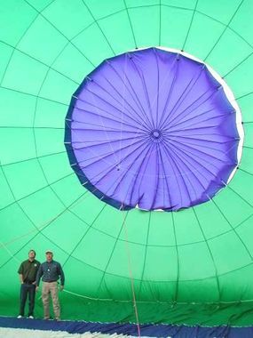 Two men stand before a purple and green hot air balloon parachute.