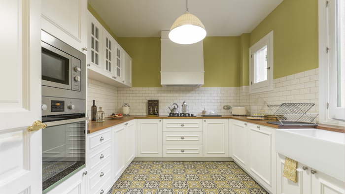 A modernized kitchen featuring a tiled floor with intricate patterns, sleek white cabinetry, and walls painted in a refreshing green hue.