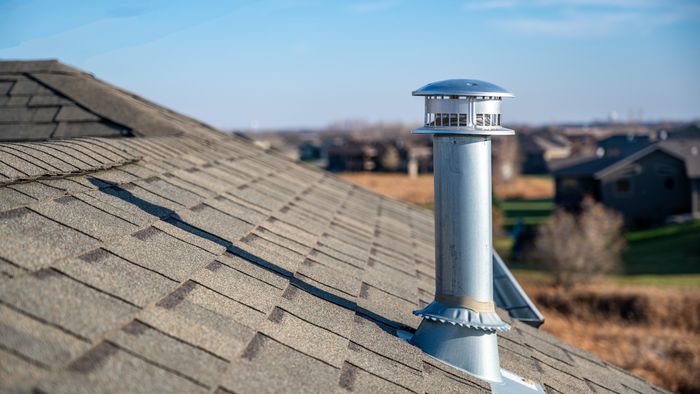 A side perspective of a metallic chimney vent installed on a shingled rooftop