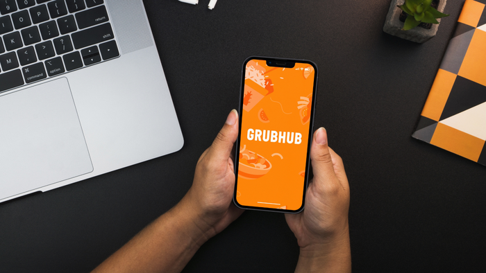 An individual holding a smartphone displaying the Grubhub logo