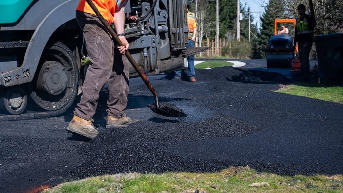 Construction worker spreading newly laid asphalt