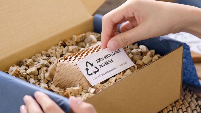 A shipping box packed with reusable packing materials, with a hand holding a card that says 'Reusable, Recyclable.'