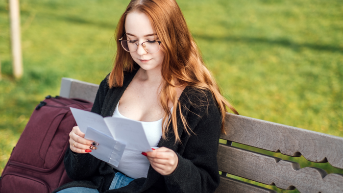 A student sitting on a bench engrossed in reading letters