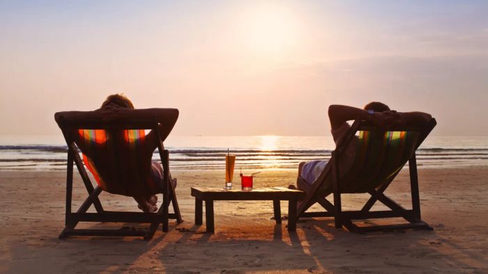 A pair enjoying a serene beach moment, seated in chairs with two cocktails on a table beside them