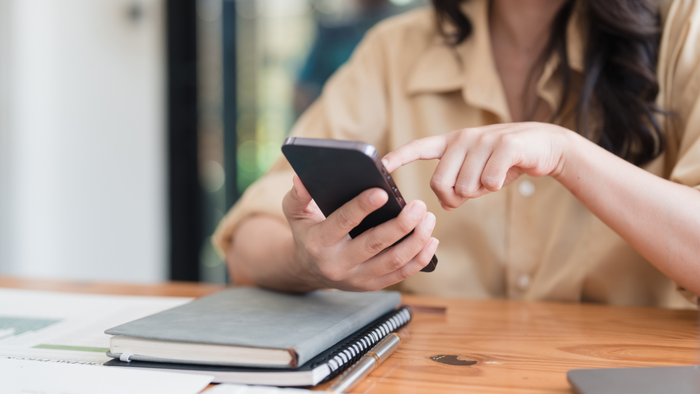 A woman reviewing her phone and jotting notes in a compact notebook
