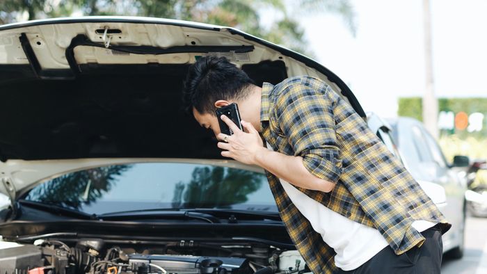 A man inspecting a car engine while using a smartphone