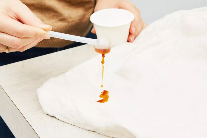 A person pouring liquid onto the corner of the Quince European Linen Duvet Cover on a table