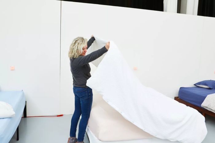 A person laying out the Quince European Linen Duvet Cover on a bed