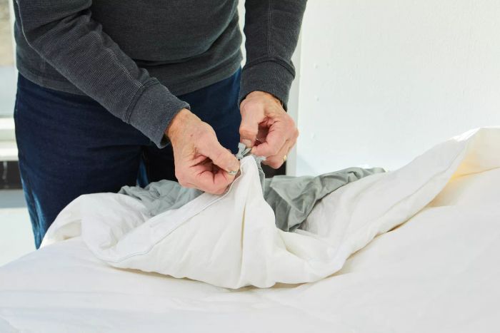 A person securing the Slumber Cloud Essential Duvet Cover with a knot on a bed