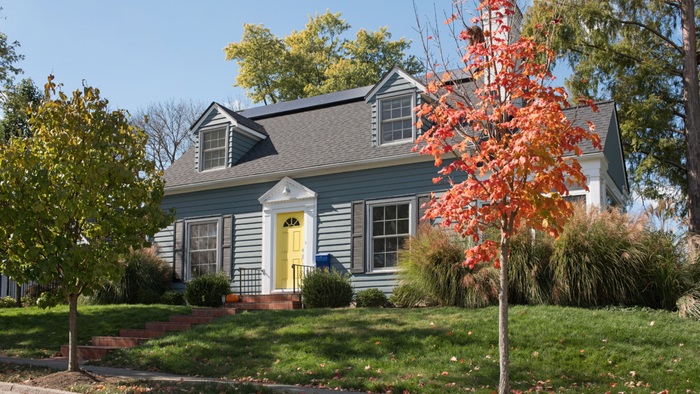 A charming blue house featuring a yellow door and a vibrant green lawn captured in a photograph.