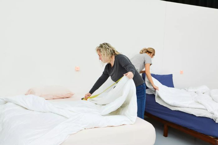 A person measuring the Quince European Linen Duvet Cover with a tape measure on a bed