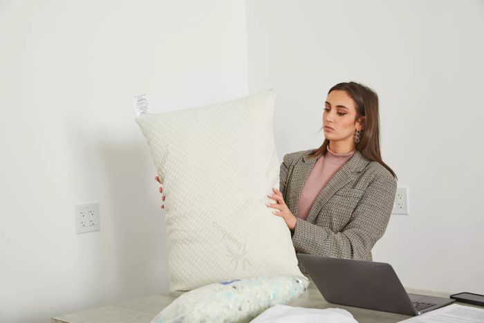A person holding a Snuggle-Pedic Adjustable Shredded Memory Foam Pillow beside a computer