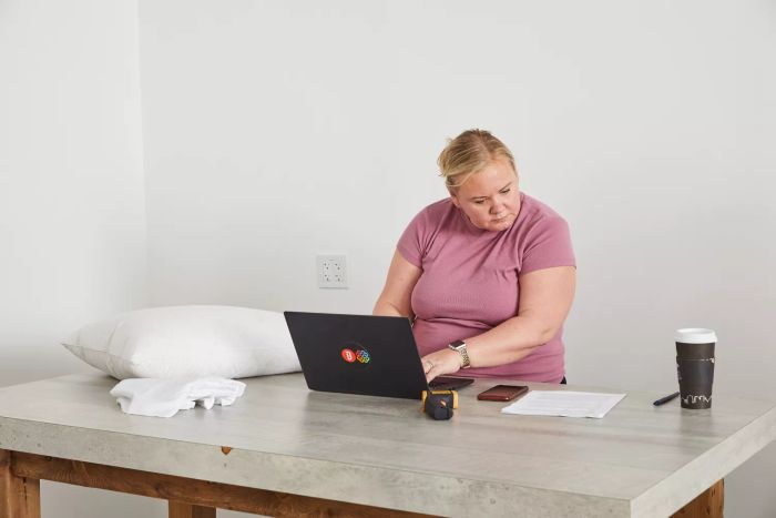 A person typing on a laptop with a Nest Bedding Easy Breather Natural Pillow placed on the table nearby
