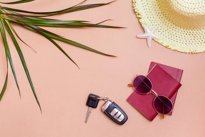 A vibrant summer travel scene, featuring sunglasses, passports, car keys, and a straw hat arranged on a soft beige surface