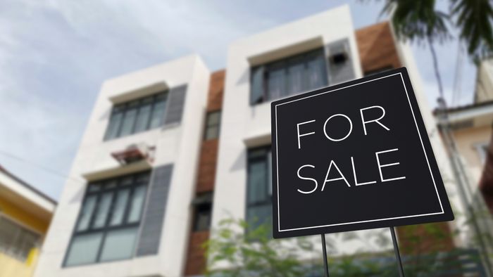 A 'For Sale' sign placed in front of an apartment building