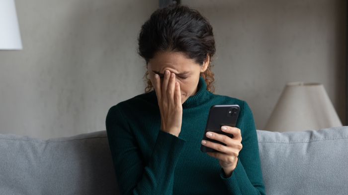 Woman reacting to unfortunate news on her phone.