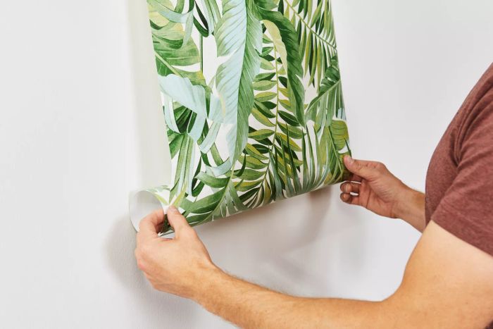 A person unrolling A-Street Prints Alfresco Palm Leaf Wallpaper onto a white wall