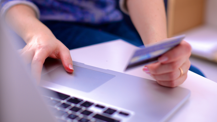 A person holding a credit card, preparing to use it while browsing on their laptop