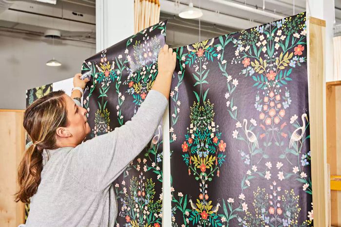A woman applies the Rifle Paper Co. Luxembourg Peel & Stick Wallpaper onto a freestanding wall with care.