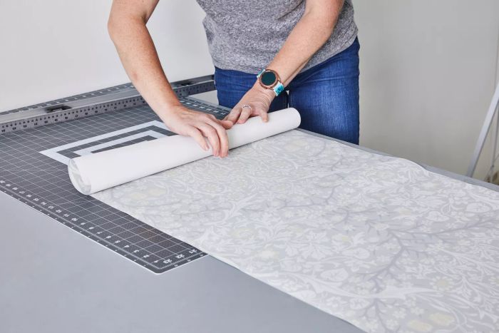 A person rolls out the Ballard Designs Juliet Floral Wallpaper on a table.