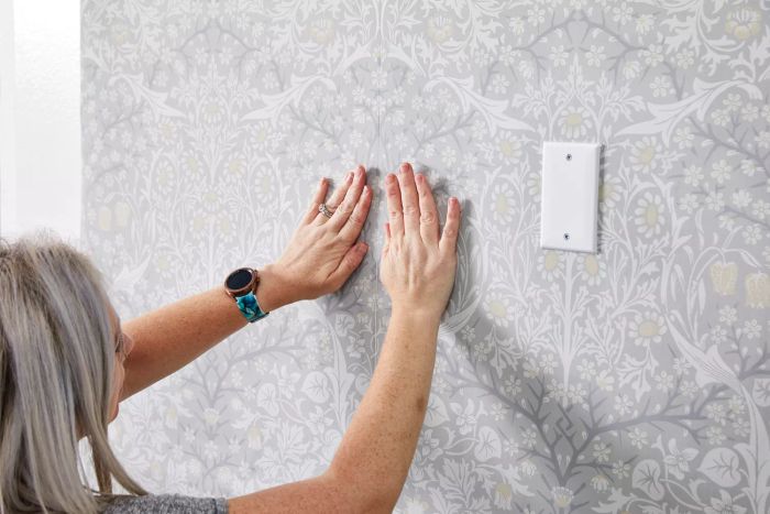 A person is touching the Ballard Designs Juliet Floral Wallpaper applied to the wall.