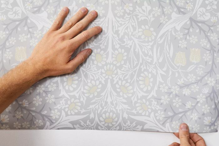 A hand holds the Ballard Designs Juliet Floral Wallpaper against a white wall, highlighting its design.