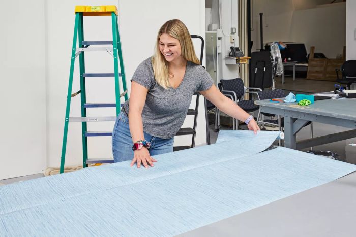 A person lays out two rolls of York Wallcoverings Nautical Living Wallpaper side by side on a table.