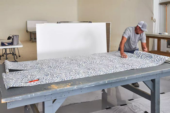 A person is shown measuring the Serena & Lily Priano Wallpaper on a table, ensuring precise placement.