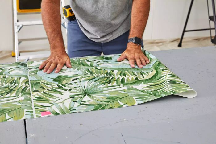 A person folding A-Street Prints Alfresco Palm Leaf Wallpaper on a table