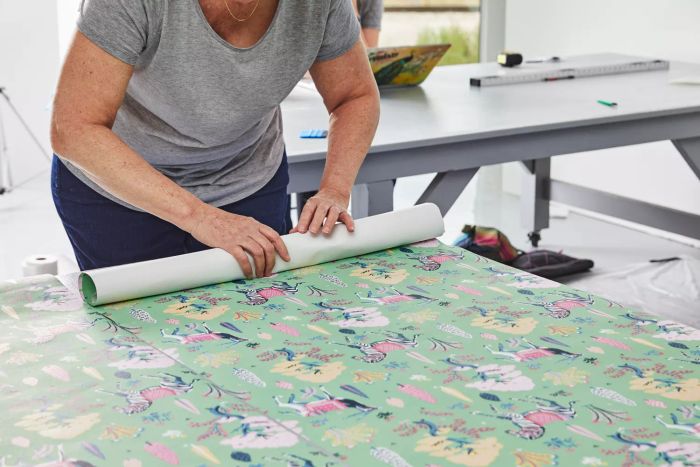 A woman is rolling out the Printfresh Antelope's Forest Wallpaper on a table.