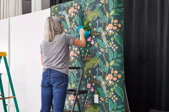 A person applying Rifle Paper Co. Peacock Wallpaper to a white wall with a sponge