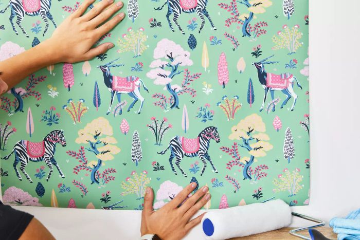 A woman holds a piece of Printfresh Antelope's Forest Wallpaper up against a white wall