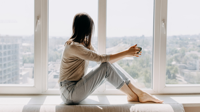 A woman sitting by a large window, staring out into the distance