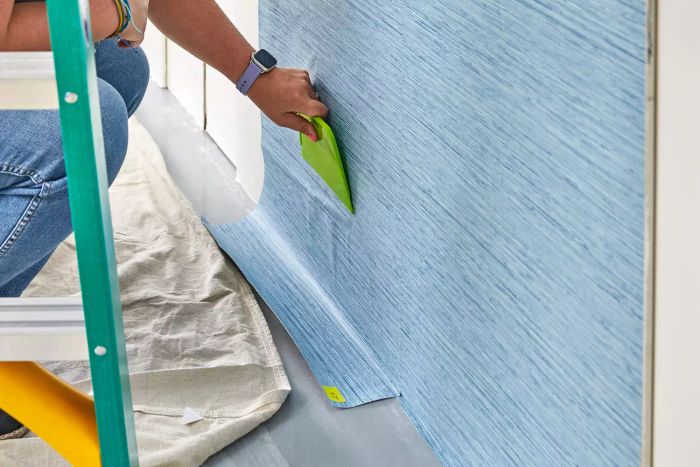 A person uses a scraper to remove York Wallcoverings Nautical Living Wallpaper from a wall.