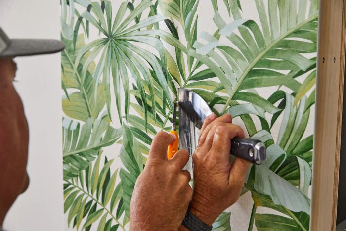 An individual scraping a section of A-Street Prints Alfresco Palm Leaf Wallpaper from the wall