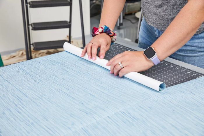 A person unrolls the York Wallcoverings Nautical Living Wallpaper on a flat surface.