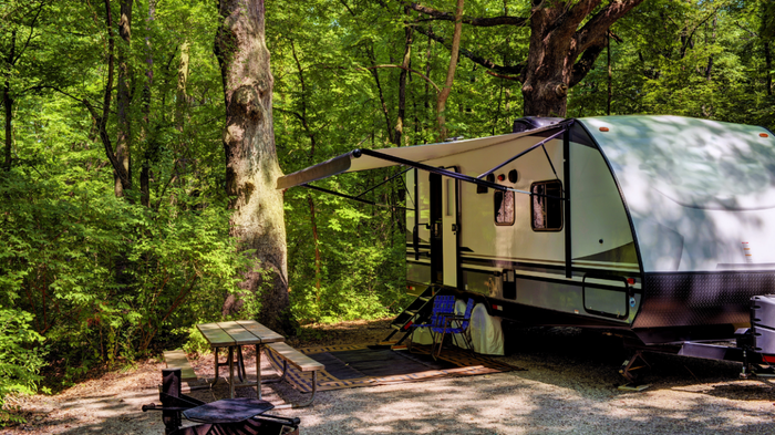 A towable RV trailer sits nestled in a tranquil forest clearing.