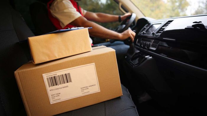 Packages resting on the passenger seat of a car with the driver in the background.