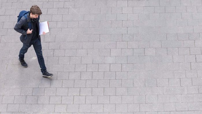 A young man with a backpack and folders walking on a paved pathway