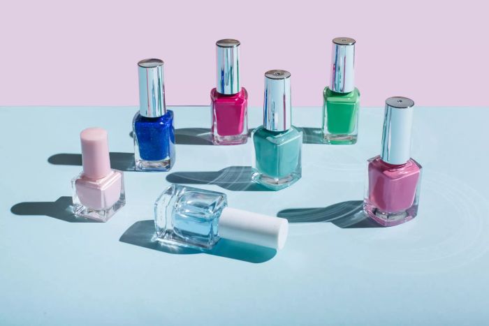 Vibrant bottles of nail polish arranged on a soft pastel blue and pink background, reflecting the manicure and pedicure theme. Flat lay, overhead shot.