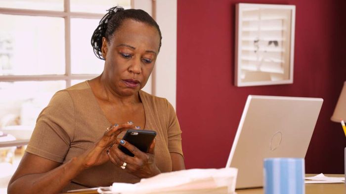 an elderly woman using a laptop and smartphone to analyze financial data