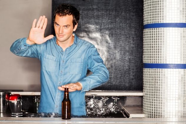 A bartender with a beer bottle gestures a stop sign at the counter.