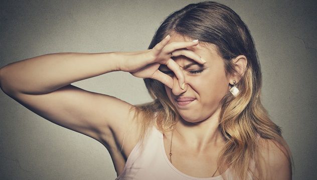 A woman pinches her nose with her fingers, looking with disgust as if something smells terrible.