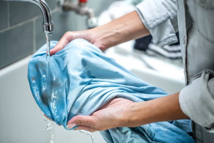 hands holding a stained piece of clothing under running water