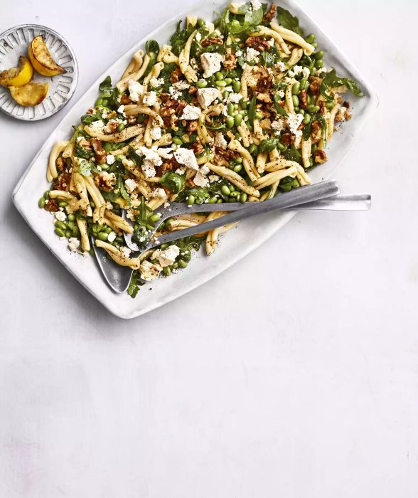 Edamame pasta salad served in a dish alongside roasted lemons