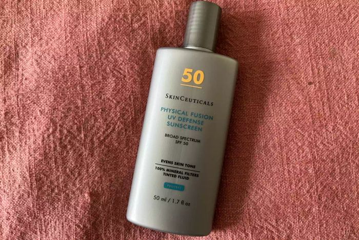 A bottle of SkinCeuticals Physical Fusion UV Defense SPF 50 displayed on a red background