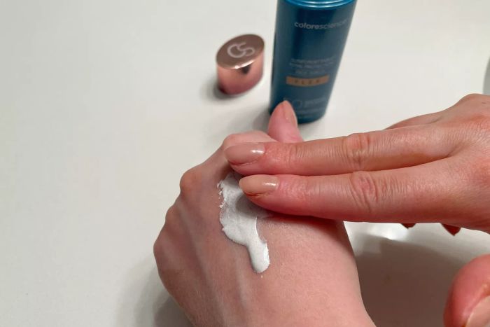 A person applying Colorescience Sunforgettable Total Protection Face Shield Flex SPF 50 to their hand